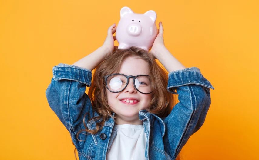 Girl with glasses holding piggy bank on top of her head
