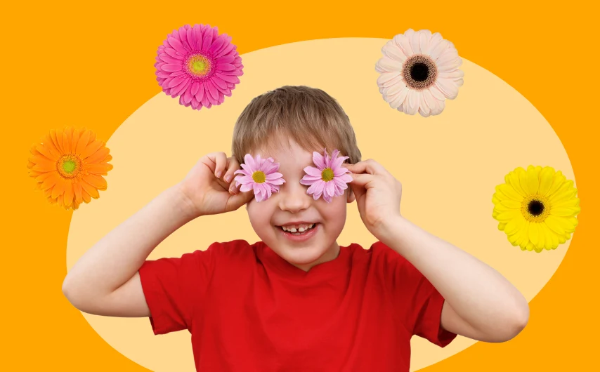 Child smiling holding flowers on their eyes