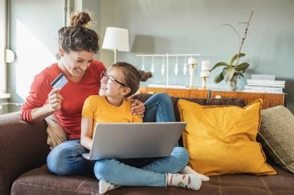 Mother with child on lap looking at each other while holding a laptop and credit card