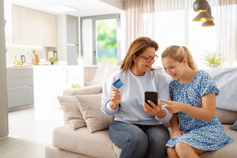 Woman and young girl looking at phone holding a credit card